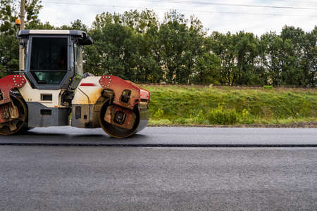 Asphalt road roller with heavy vibration roller compactor press new hot asphalt on the roadway on a road construction site. Heavy Vibration roller at asphalt pavement working. Repairing.の写真素材
