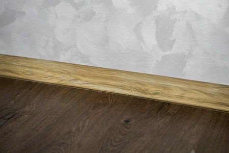 Laminate with plastic baseboard with a wooden texture. Newly installed wooden laminate flooring and baseboards in home. Modern design. Close up of plastic plinths on dark wooden oak floor parquet.の写真素材