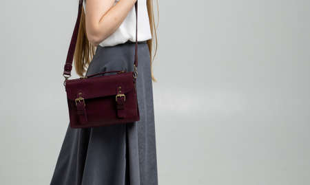 Small red leather bag over a woman shoulder on a white background. Shoulder handbag. Woman in a white shirt and grey skirt and with a red handbag. Style, retro, fashion, vintage and elegance.の写真素材