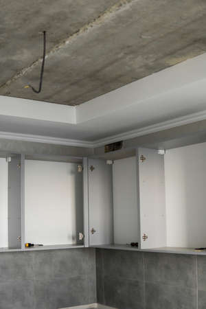 Custom kitchen cabinets installation without a furniture facades mdf. Gray modular kitchen from chipboard material on a various stages of installation in kitchen with a grey tile on floor and walls.の写真素材