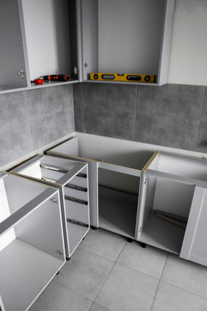 Custom kitchen cabinets installation without a furniture facades mdf. Gray modular kitchen from chipboard material on a various stages of installation in kitchen with a grey tile on floor and walls.