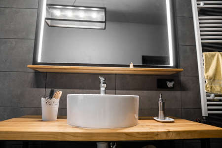 Bathroom interior with grey tile on a wall, stylish round sink and tap on a oak wood worktop. Minimalism in interior of bathroom.の写真素材