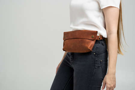 Girl in a white blouse with a leather red handmade bag over her waist. Designer dark brown banana bag. Woman in a studio. Comfortable small bag for walking.の写真素材
