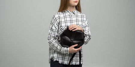Small black leather bag in a womans hand on a white background. Shoulder handbag. Woman in a white...