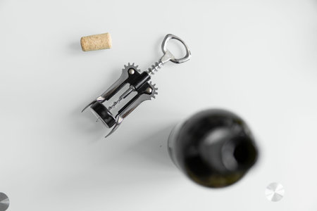 Metal corkscrew in a mans hand with a bottle of red wine on a background with a light white kitchen. Wine lover. Wine opener.の写真素材