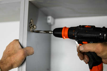 The master drills a wooden plate from chipboard with a drill on a kitchen cabinet.の写真素材