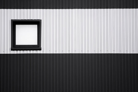 Black and white corrugated iron sheet used as a facade of a warehouse or factory with a window....