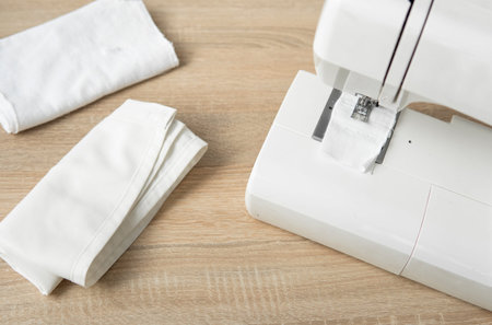 Sewing machine with with a white cloth on a wooden table.