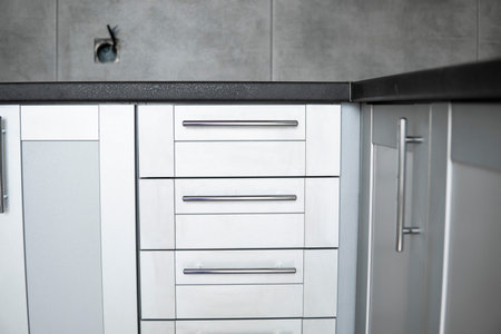 Modern minimalist style kitchen close up in monochrome tones. Custom kitchen with grey white facades mdf and dark grey countertop. Modular kitchen from chipboard.