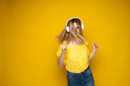 Beautiful attractive young blond woman wearing yellow t-shirt and glasses in white headphones...