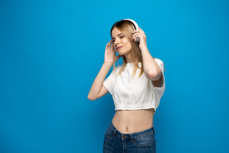 Beautiful attractive young blond woman wearing white t-shirt and glasses in white headphones...