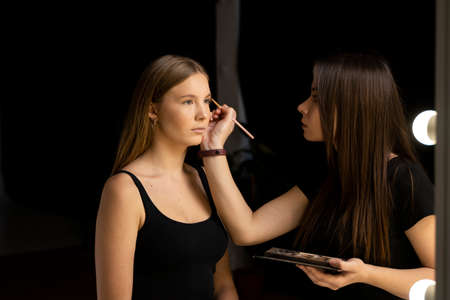 Makeup artist doing a eyebrows makeup on a beautiful woman face. Hand of make-up master is painting eyebrow of young beauty model girl. Make up in process.の写真素材