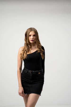 Beautiful young woman portrait in a black t-shirt and mini skirt. Studio shot, isolated on gray background.の写真素材