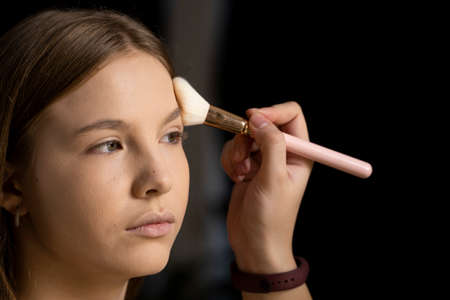 Close up face of beautiful young woman getting powder on her cheek with a brush. Professional makeup artist.の写真素材
