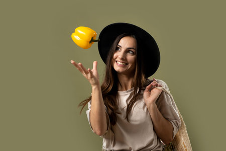 Smiling brunette young woman in a beige t-shirt and a hat holding a reusable mesh bag with fresh...