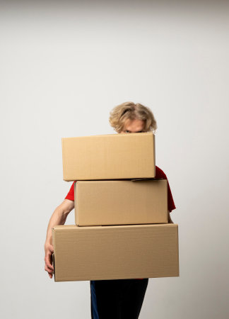 Delivery man in a red uniform holding a stack of cardboard boxes. Courier delivering postal packages over white studio background.の写真素材
