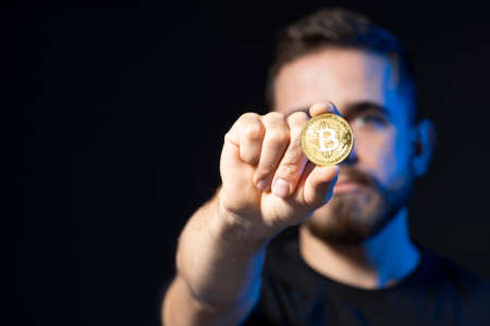 Confident young business man wearing black with a bitcoin in a hand.の写真素材