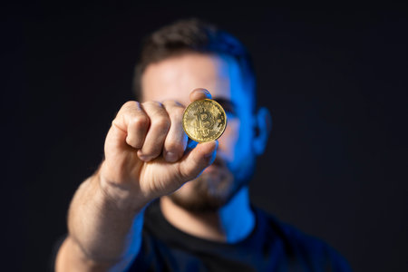 Mature bearded man wearing in black t-shirt holding gold bitcoin in hand and standing isolated on black background.の写真素材