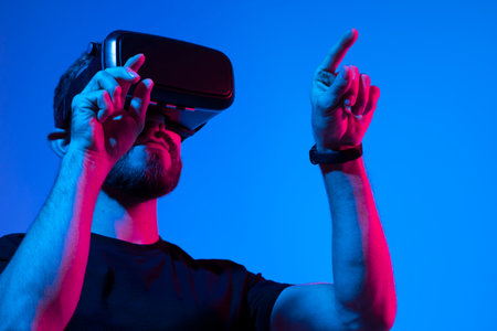 Young bearded man in virtual reality helmet plays online game in metaverse. Game simulates behavior in fictional world, gadgets and virtual reality addiction. Future technology concept.の写真素材