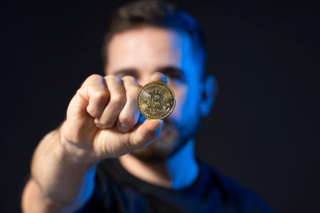 Young bearded man holding virtual currency bitcoin coin. Crypto trader holding a btc coin. Cryptocurrency.の写真素材