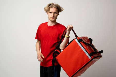 Delivery employee man in red t-shirt uniform work as dealer courier and hold red thermal food bag with food isolated on white background studio. Service concept.の写真素材