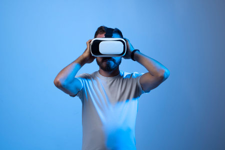 Young bearded guy in VR goggles touching air and excited with new feelings in dark neon lights.