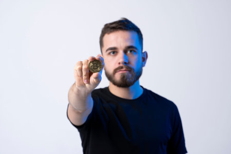 Successful young business man in black t-shirt with bitcoin coin isolated on grey background in...