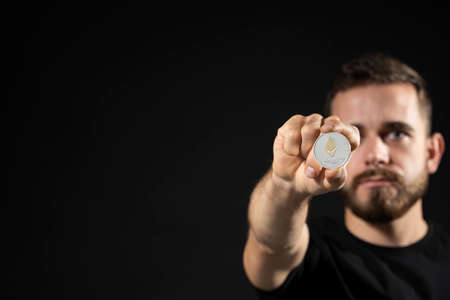 Successful business man in black t-shirt with ethereum coin isolated on grey background in studio with copy space. Hold ethereum, future currency.の写真素材