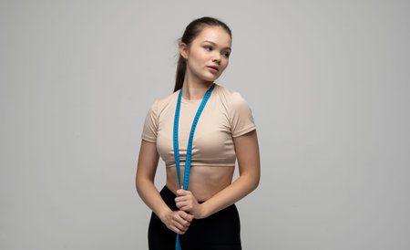 Attractive young brunette woman in sportswear with blue measuring tape around her neck looks in a...