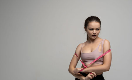 Weight loss and diet concepts. Brunette woman in sportswear holding pink measuring tape around her...