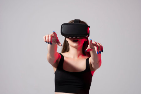 Brunette woman in a black t-shirt and VR headset looking up and trying to touch objects in virtual...