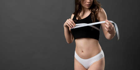 Cropped image beautiful young brunette woman 20s in black and white underwear standing posing measuring breast with measure tape isolated on black wall background.の写真素材