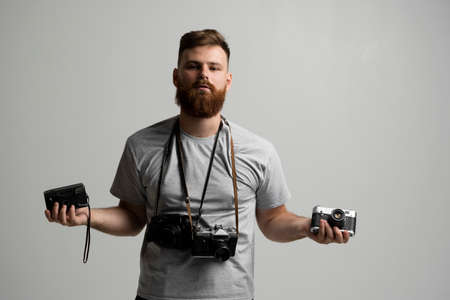Portraite of professional handsome bearded male photographer with bunch of vintage photo cameras in photo studio, isolated on white background.の写真素材
