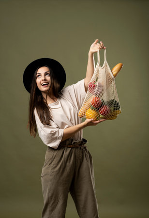 Eco friendly shopping. Smiling young woman holding string reusable mesh bag with organic fruits and...
