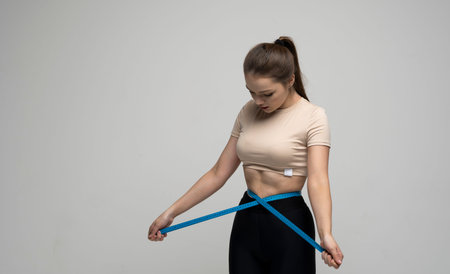 Attractive young brunette women in sportswear and takes measurements of her waist. Measurements of a...