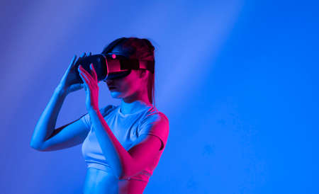 Woman experiencing virtual reality goggles in neon light.の写真素材