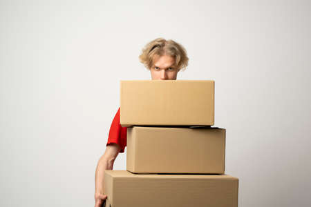 Young delivery man standing with lot of parcel post boxes isolated over white background.の写真素材