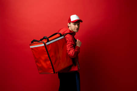 Delivery courier with red food backpack deliver food orders. Man delivering fast food with thermal backpack. Food delivery courier.の写真素材