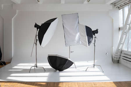 Professional lighting equipment, flashes, c-stands on a cyclorama in modern photo studio with a huge windows. Octabox, stripbox, softbox, buety plate and other stuff for photography.の写真素材
