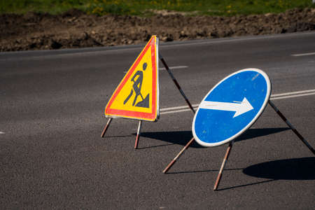 Road signs indicating the repair of asphalt and the direction to bypass the dangerous section. Repair work in the middle of the carriageway, selective focus.の写真素材