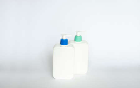 Two white cosmetic plastic bottle with pump dispenser pump and blue cap on white background. Liquid container for gel, lotion, cream, shampoo, bath foam.の写真素材