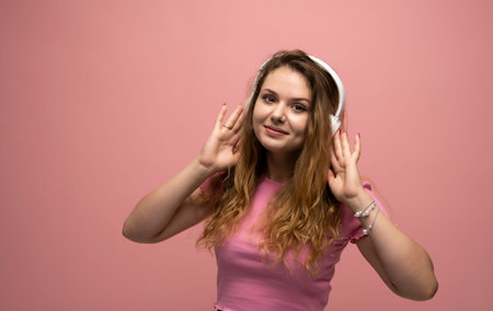 Young woman listening music in headphones with a smile face and stand over pink background....