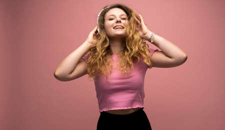 Young woman listening music in headphones and dancing with a smile face and stand over pink background. Attractive lady enjoying song copy space.の写真素材