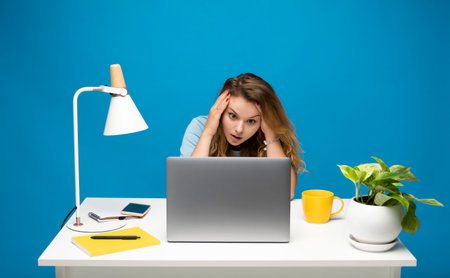 Young confused disappointed troubled freelancer woman at white desk with laptop computer.