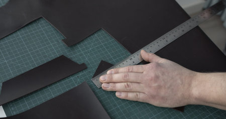 Leather craftsman working with brown natural leather work with knife and metal ruler and cutting a...