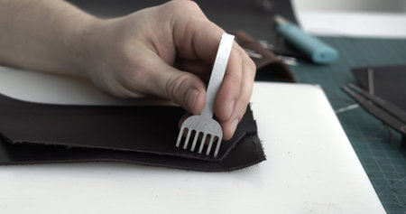 Close up mens hands make a leather product. Punching holes in the leather with a hole punch with a...