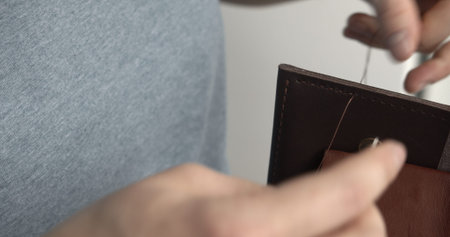 Making a handmade brown leather wallets. The hands of the master sew a leather product.