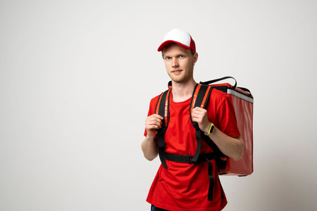 Delivery man in a red uniform carry thermal backpack full of food, groceries to the clients. Food delivery service.の写真素材