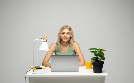 Portrait of attractive freelancer woman in a green t-shirt with a laptop in a studio with a white wall.の写真素材