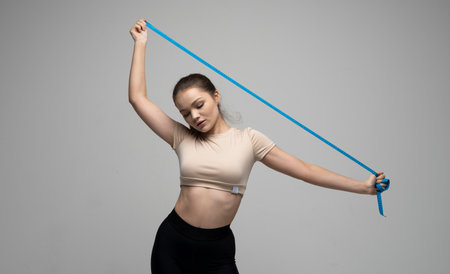 Attractive brunette woman in sportswear holding a blue measuring tape. Weight loss and diet concepts. Health care and healthy nutrition. Perfect slim body.の写真素材